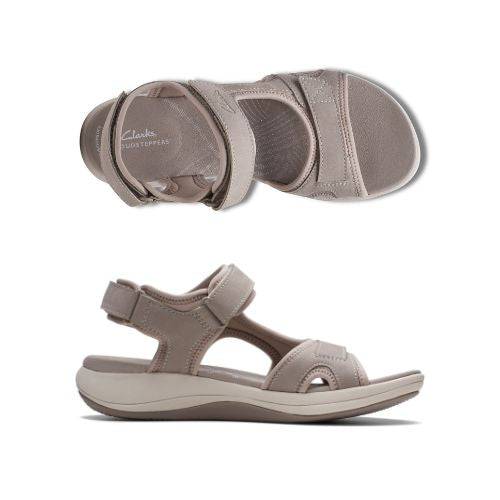 Top and profile view of Stone color walking sandal with Velcro on heel, toe and ankle strapes. Light beige thick midsole and darker beige rocker rubber outsole. Tan footbed has white Clarks logo stamped with wave designs across beige lining