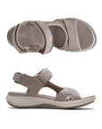 Top and profile view of Stone color walking sandal with Velcro on heel, toe and ankle strapes. Light beige thick midsole and darker beige rocker rubber outsole. Tan footbed has white Clarks logo stamped with wave designs across beige lining