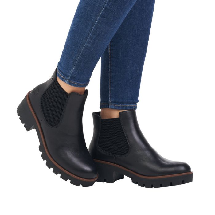 Legs in jeans wearing black leather Chelsea boot with platform outsole.