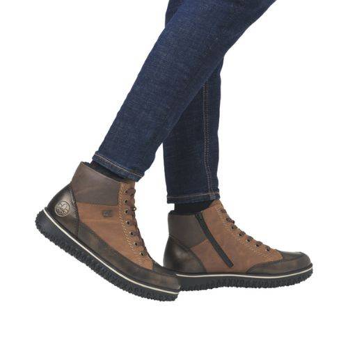 Woman in dark blue jeans wearing Rieker brown and grey lace up sneaker boots with a black outsole.