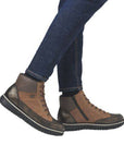 Woman in dark blue jeans wearing Rieker brown and grey lace up sneaker boots with a black outsole.