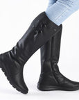 Women in light blue jeans wearing tall black leather Rieker boots with two buttons.