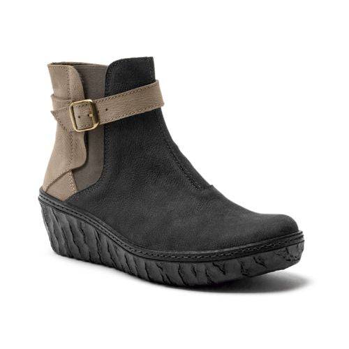 Ankle height wedge bootie with a black and taupe leather upper and black rubber outsole. There is a decorative taupe leather strap around the ankle with an adjustable gold buckle. 