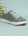 Sage green sneaker with white laces on a teal background featuring a leaf.