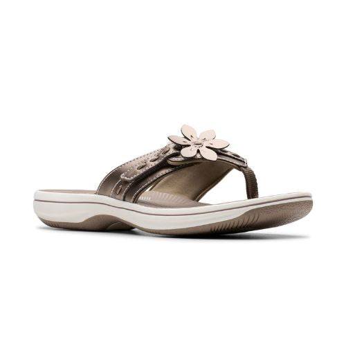 Bronze thong sandal with white midsole, bronze footbed with white designs including Clarks Cloudsteppers logo, fabric toe post, and adjustable bronze strap with bronze flower. Bronze outsole with rocker bottom design.