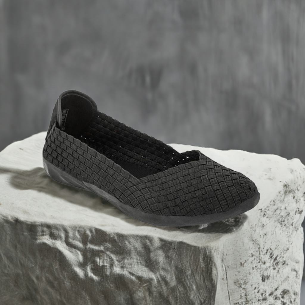 A black Bernie Mev ballet flat on a cement block.