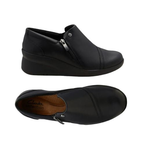 Top and Profile of Black leather wedge ankle slip-on shoe. Has a detailed silver button above side zipper. Small detailed diagonal stitching on toe. Padded tan footbed has the black Clarks logo at heel