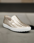 A gold leather slip on shoe with mix of woven and smooth leathers on a white outsole.