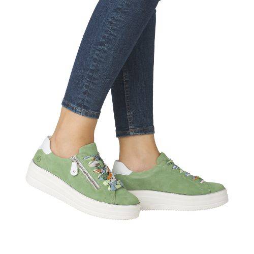 Legs of woman with jeans in green side zipper lace sneakers and white platform.