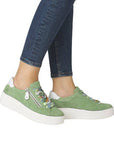 Legs of woman with jeans in green side zipper lace sneakers and white platform.