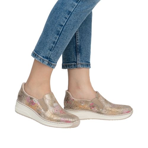 Legs of women in blue jeans with gold and pink scale pattern slip on shoes.