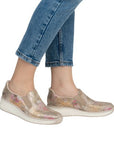 Legs of women in blue jeans with gold and pink scale pattern slip on shoes.