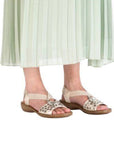 Legs of girl in light green pleated dress wearing gold sequined back strap sandals.