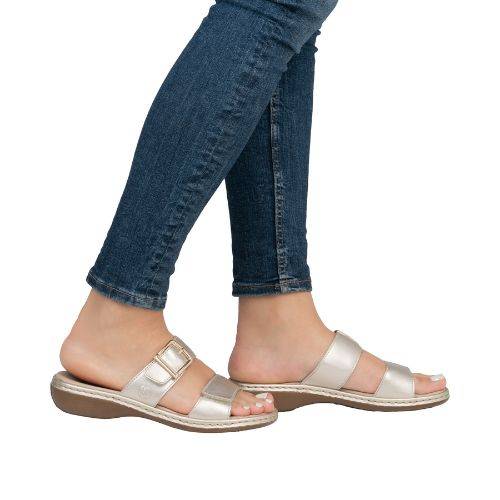 Legs of women in blue jeans wearing Rieker gold two strap slide sandals.