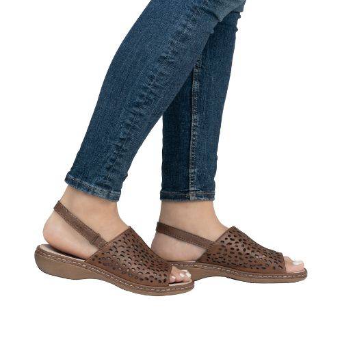 Woman in blue jeans wearing brown leather backstrap sandal with perforated upper and brown outsole.