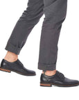 Man in grey pants wearing black leather lace-up Rieker dress shoes.