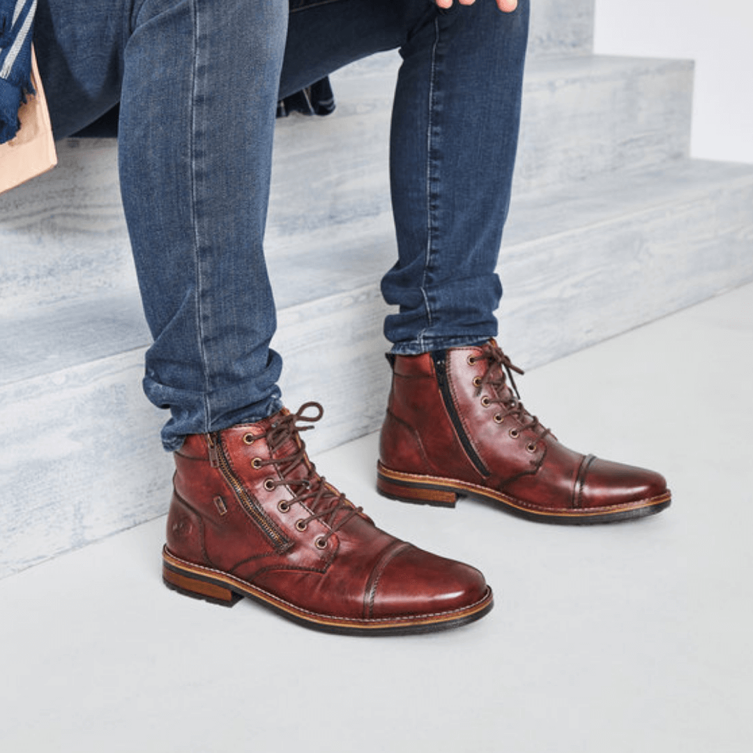 Man sitting on stairs in jeans focus point on dress boots with laces and zipper in a red/brown leather