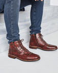 Man sitting on stairs in jeans focus point on dress boots with laces and zipper in a red/brown leather