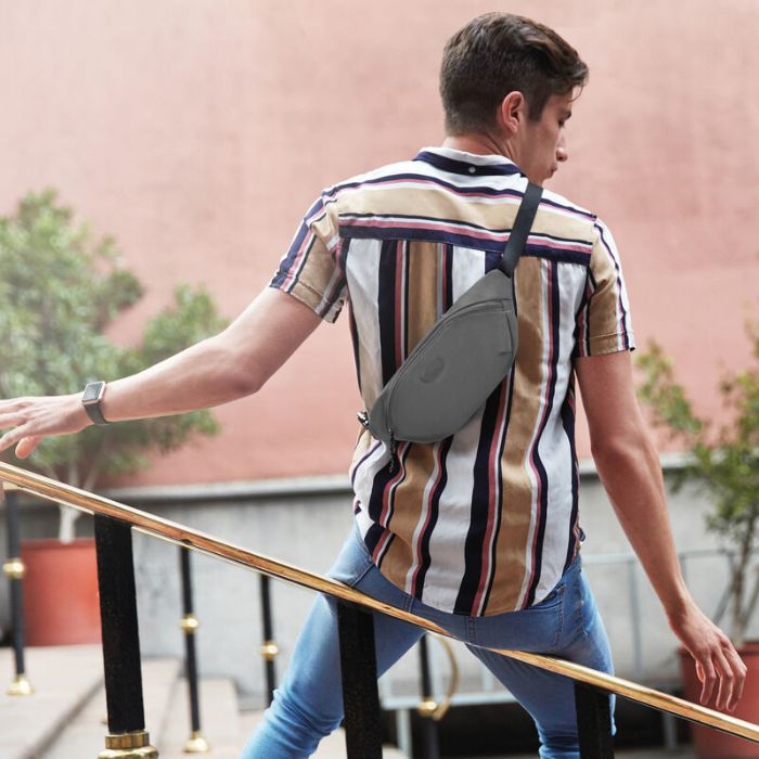 Man in striped shirt wearing a grey fanny pack as a crossbody bag. Bag has zippered closure and Travelon emblem on front.