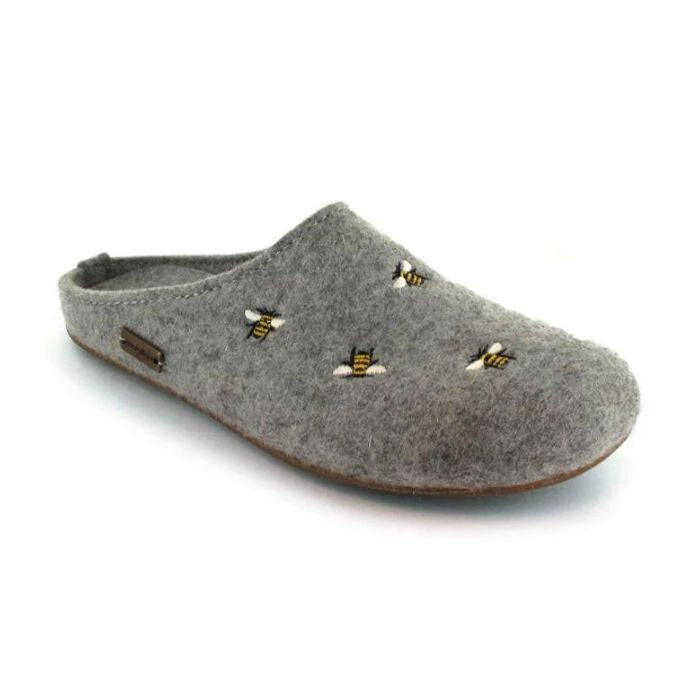 An open-back slipper with a light grey wool upper featuring small embroidered bumblebees. A brass badge with the Haflinger logo is visible near the heel. 