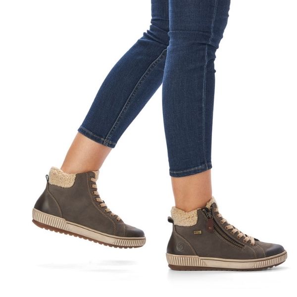 Women in jeans wearing grey sneaker boot with faux fur cuff and beige outsole.