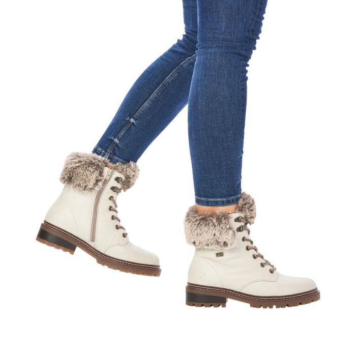 Legs in jeans wearing white leather lace-up boot with faux fur cuff and brown outsole.