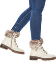 Legs in jeans wearing white leather lace-up boot with faux fur cuff and brown outsole.