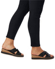 Legs in black jeans wearing black leather slide wedge sandal with bow.