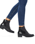 Legs wearing black and black patent patchwork ankle boot with lace closure.