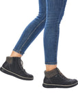 Women in blue jeans wearing black Rieker sneaker boots.