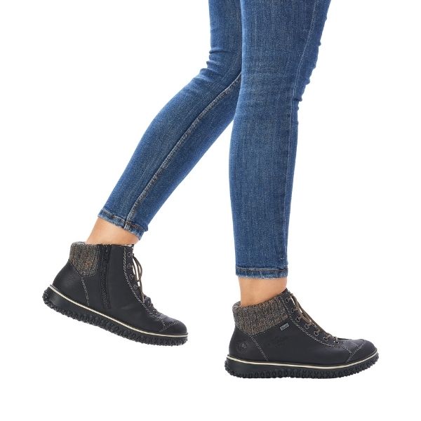 Women in blue jeans wearing black Rieker sneaker boots.